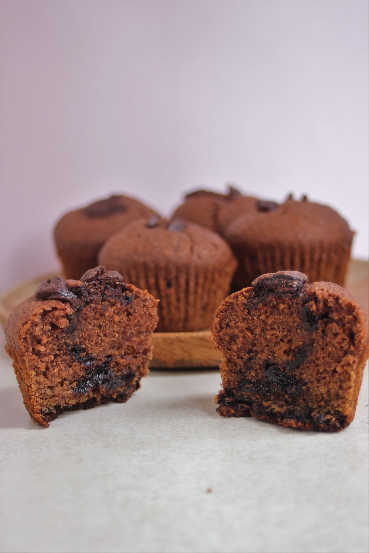 A chocolate banana muffin cut in half, seen from the front. More muffins behind on a wooden plate.