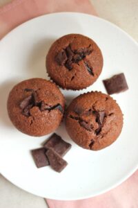 Three banana chocolate muffins on a white plate seen from above.