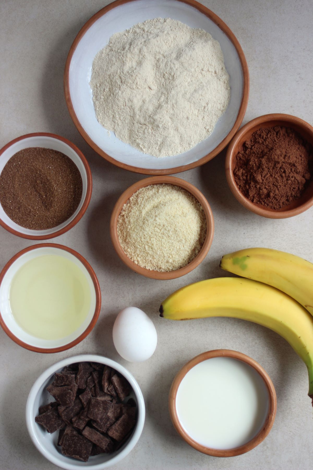 Chocolate banana muffins ingredients on different plates seen from above.