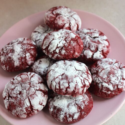 Many red velvet crinkle cookies on a pink plate.