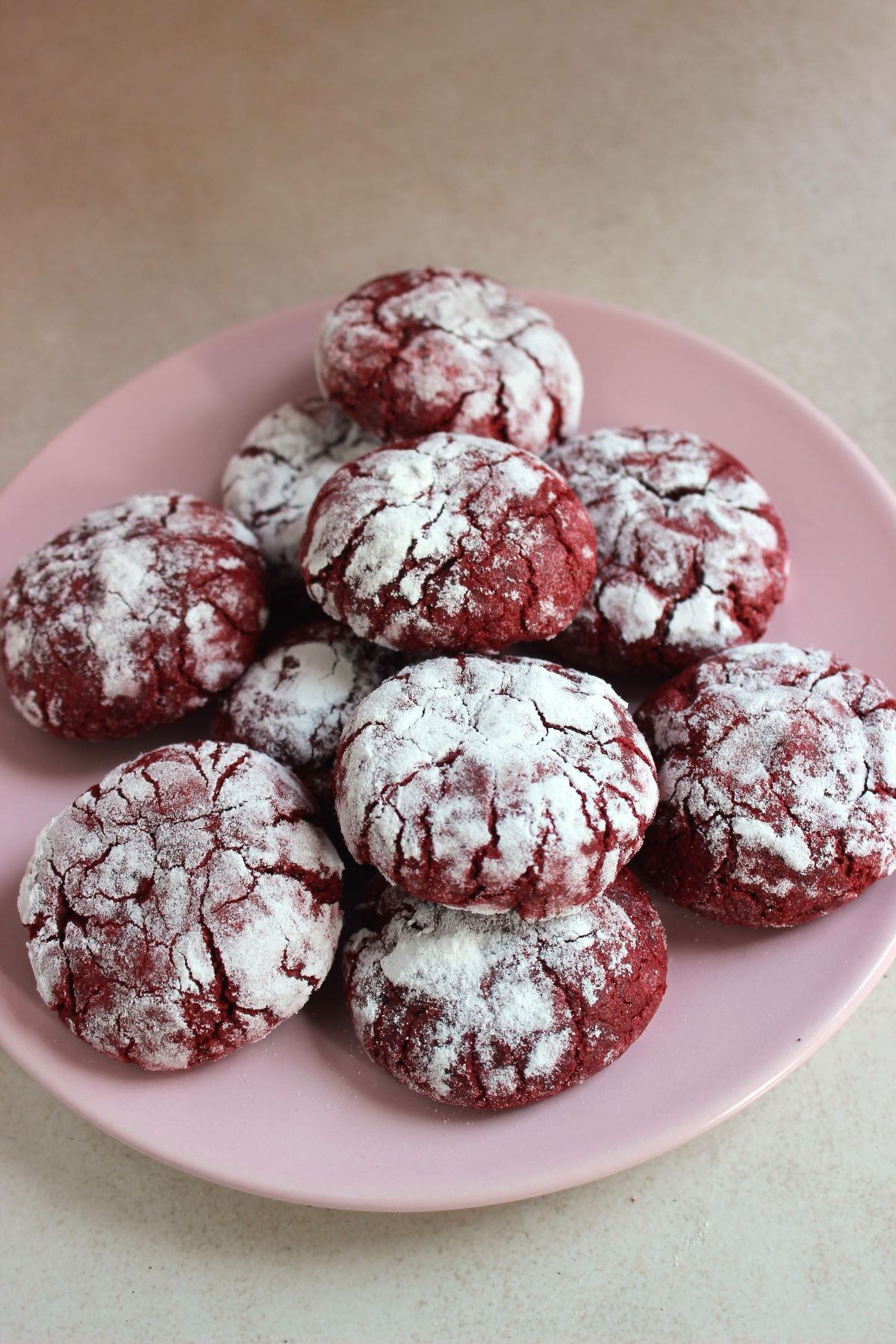 Many red velvet crinkle cookies on a pink plate.