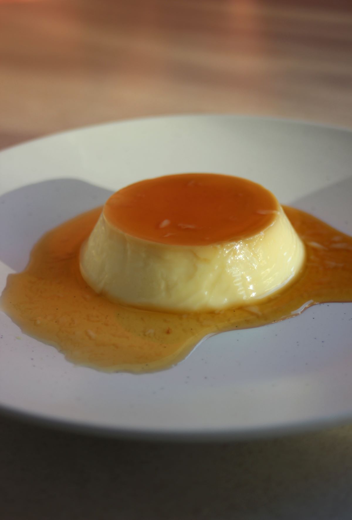 A flan with caramel on a white plate.