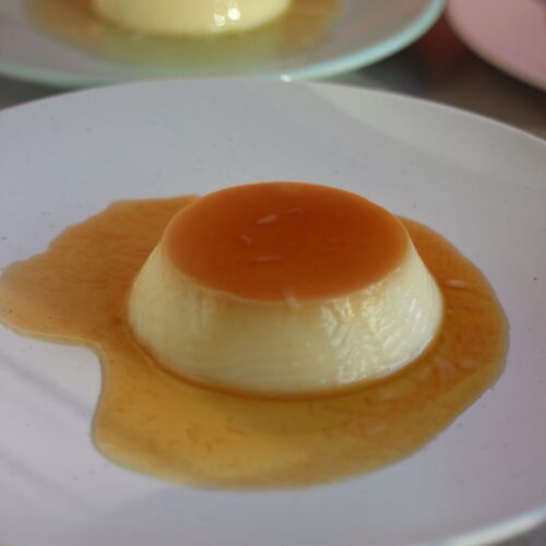 Flan with caramel on a white plate. Another plate with a flan behind.