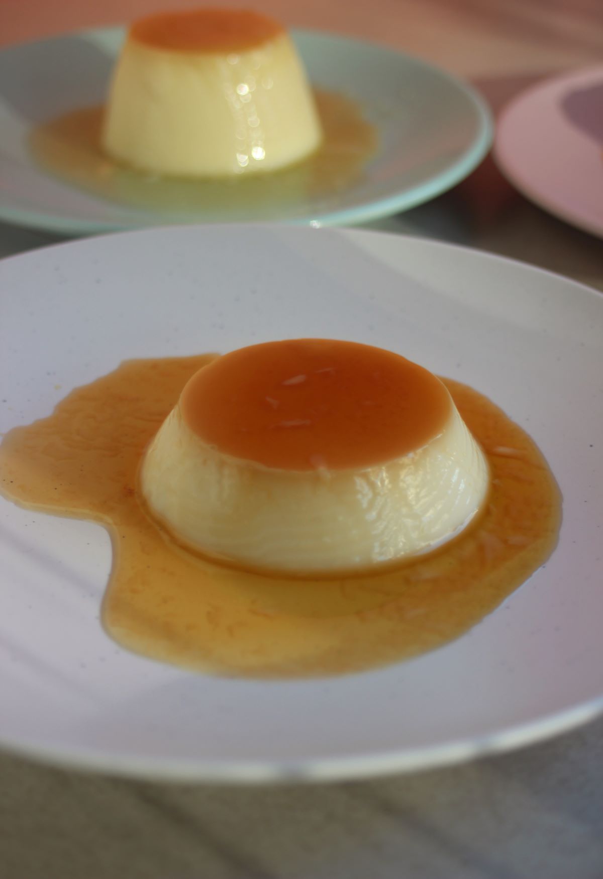 Flan with caramel on a white plate. Another plate with a flan behind.