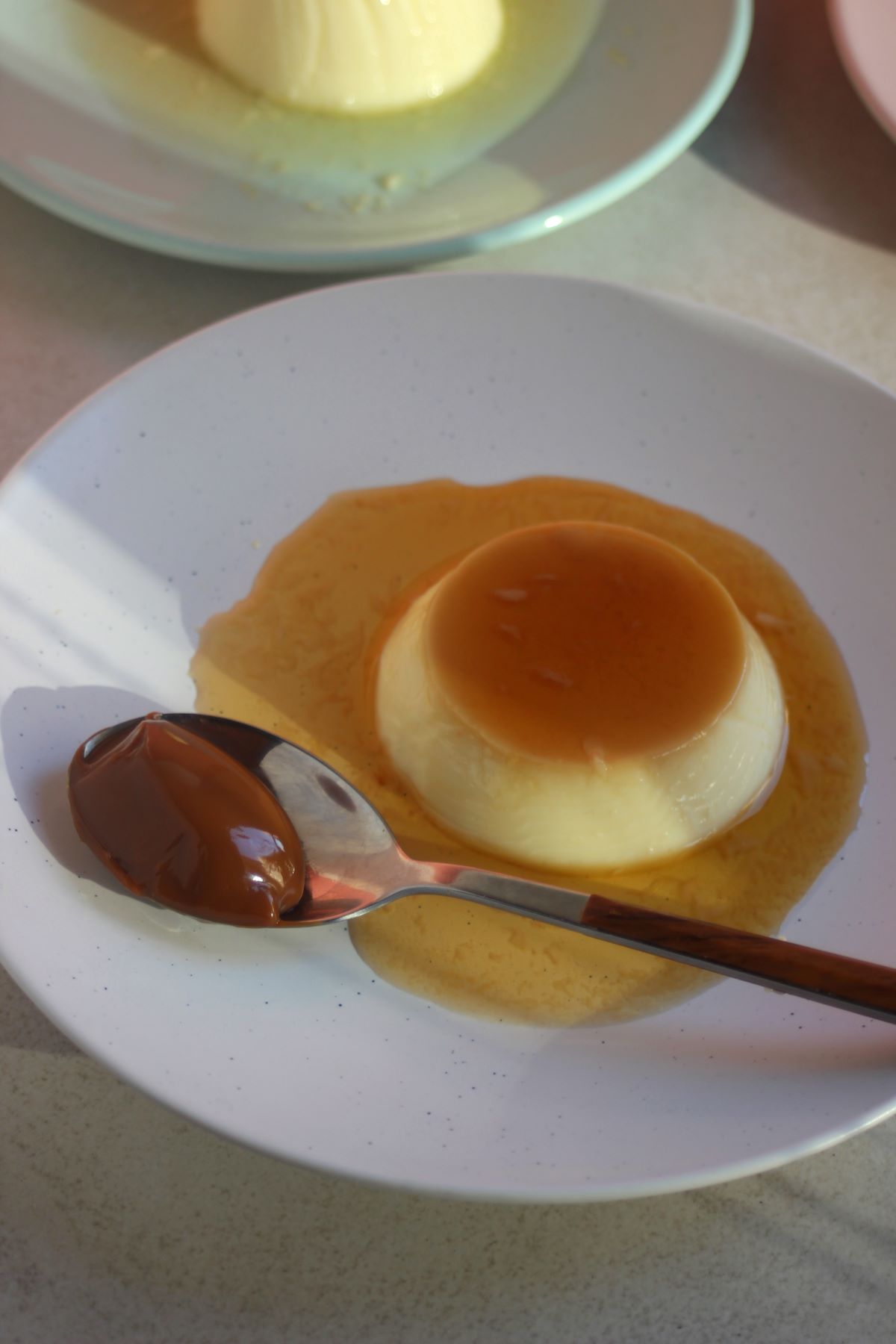 Flan with caramel and a spoon with dulce de leche on a white plate.