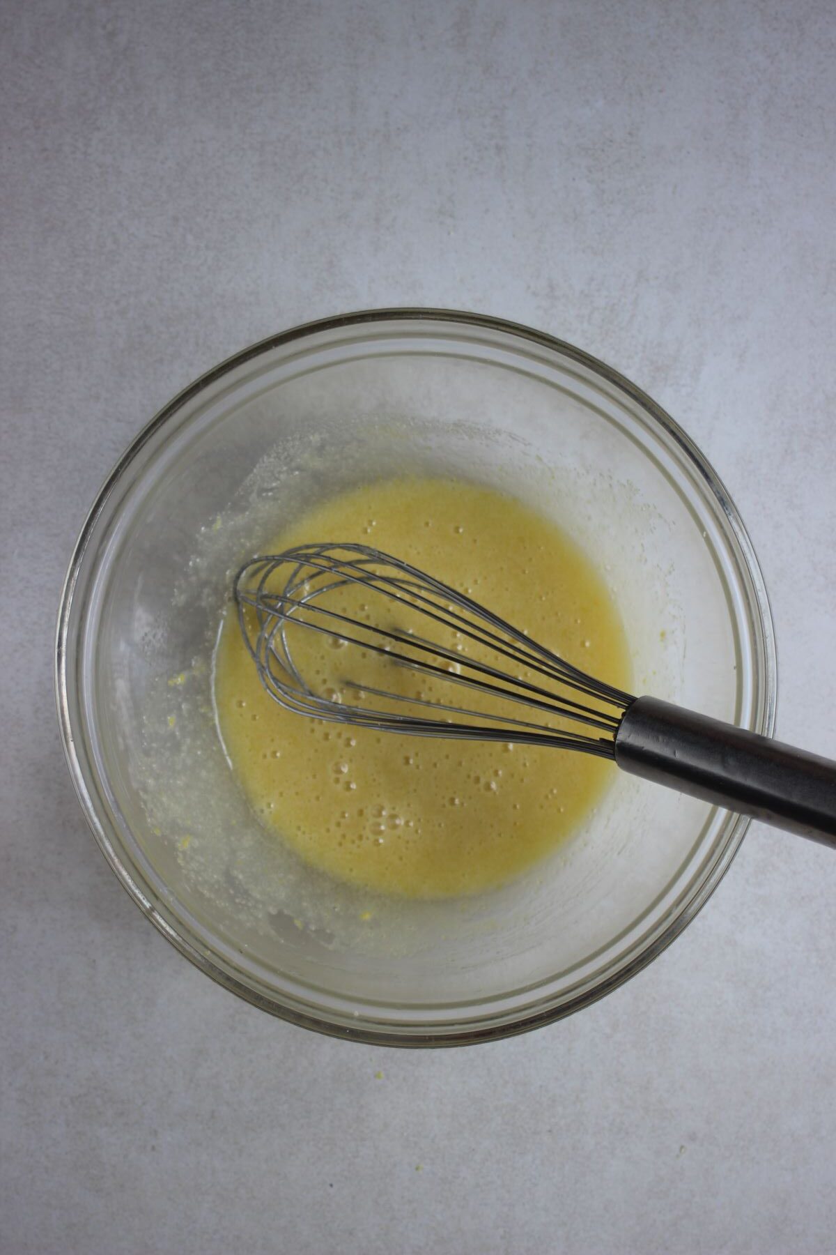 Glass bowl with a yellow liquid and a hand whisk.
