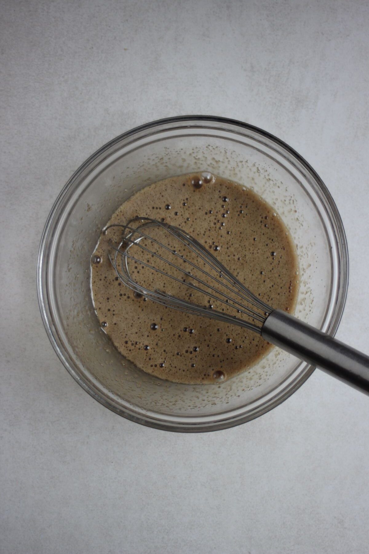 Glass bowl with a brown liquid and a hand whisk.