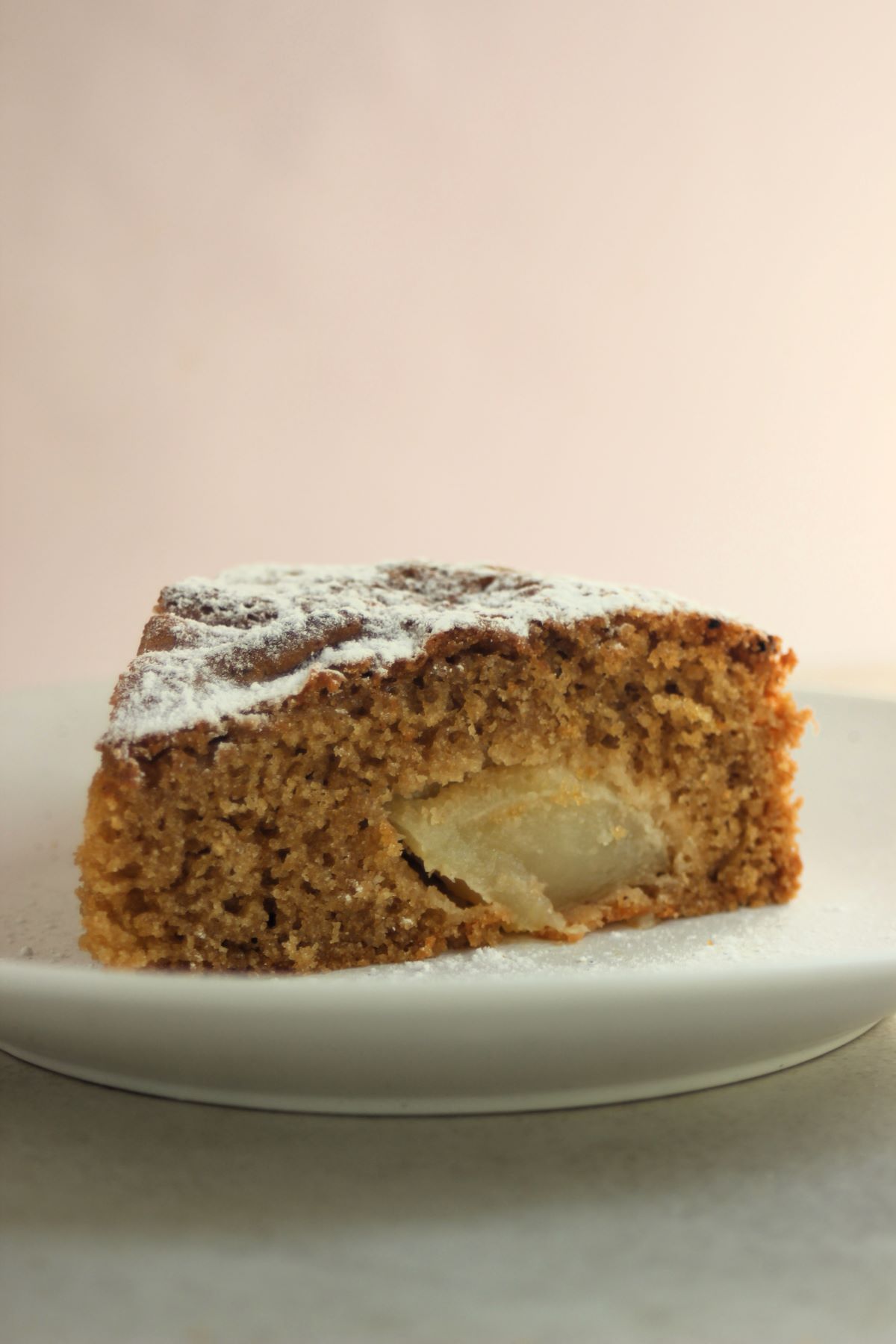 A portion of apple cake sprinkled with powdered sugar on a white plate.