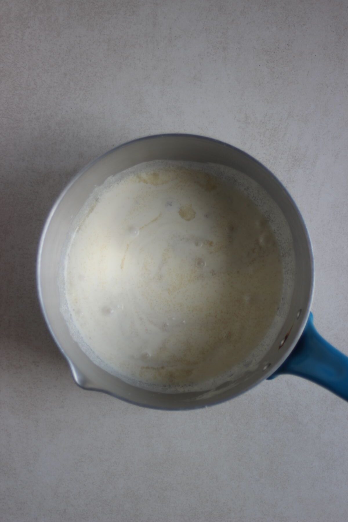 Deep saucepan with milk and sugar on a white surface.