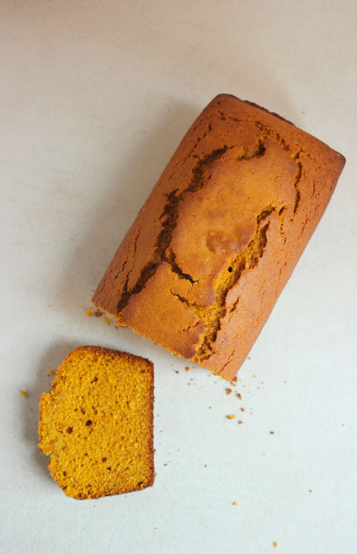 A pumpkin bread and a slice of it on a white surface seen from above.