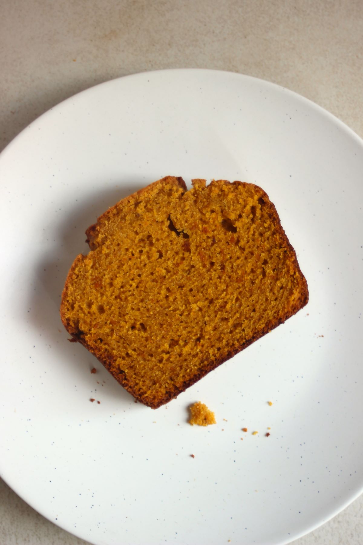 A slice of pumpkin bread on a white plate seen from above.