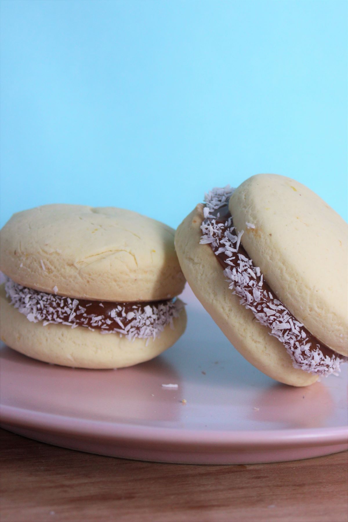 Two "alfajores" with dulce de leche on a pink plate. Ligh blue background.