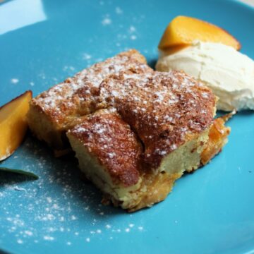 A portion of peach cake with whipped cream and peach slices on a turquoise plate.