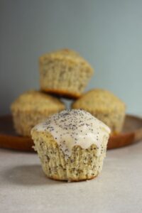 Lemon muffin with icing and poppy seeds. More muffins behind.
