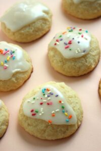 Ricotta cookies with icing and sprinkles on a light orange surface.