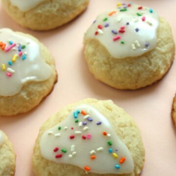 Ricotta cookies with icing and sprinkles on a light orange surface.
