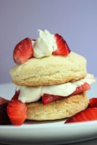 Strawberry shortcake on a white plate and strawberries on the sides.