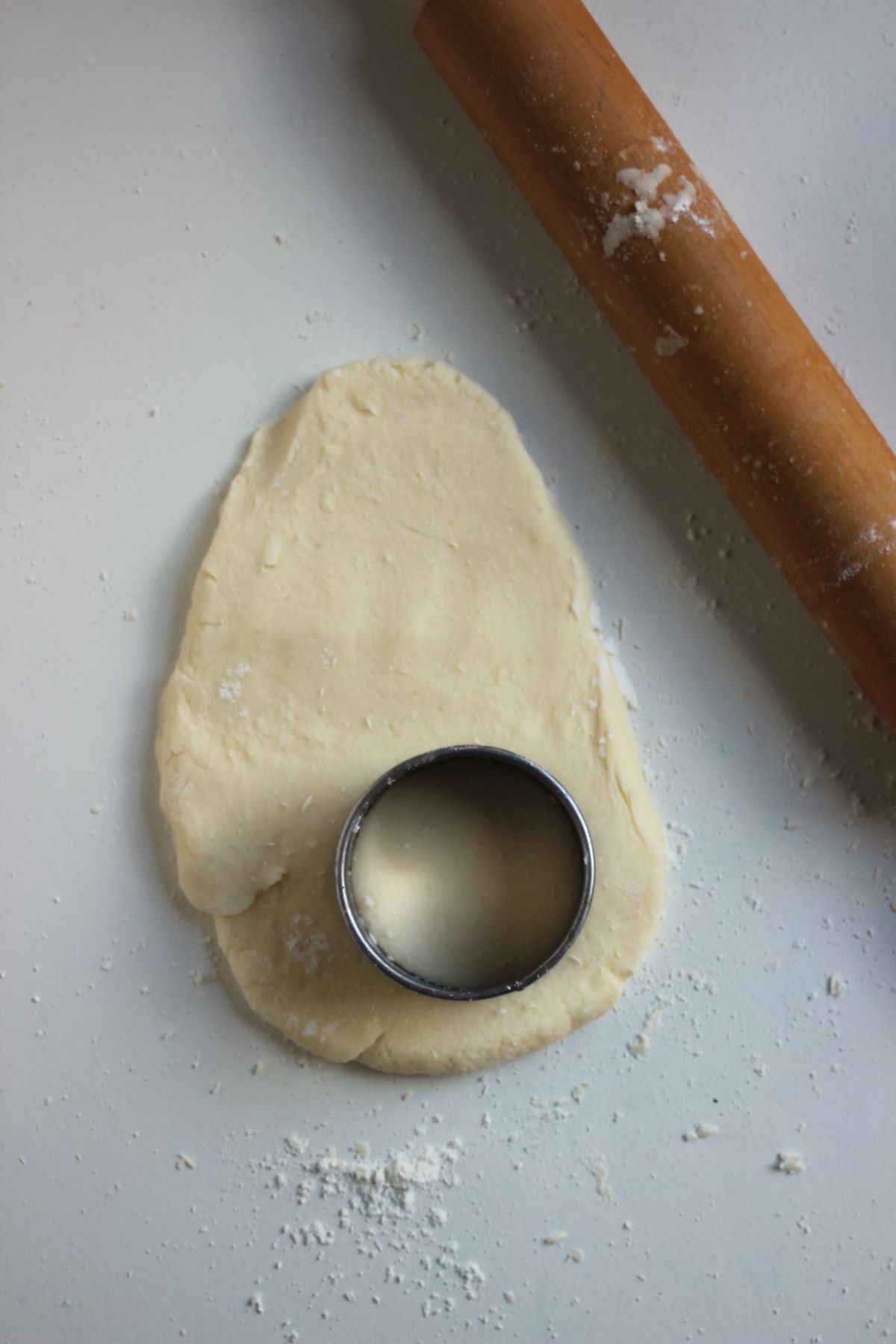 The stretched shortcake dough on a surface. A round biscuit cutter on the dough and rolling pin on the side.