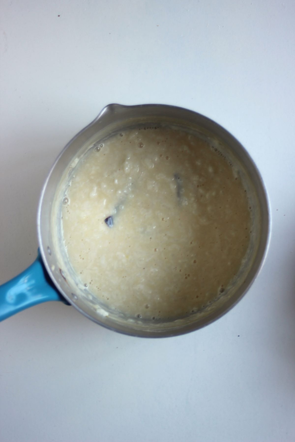 Deep saucepan with caramel rice pudding on a white surface.