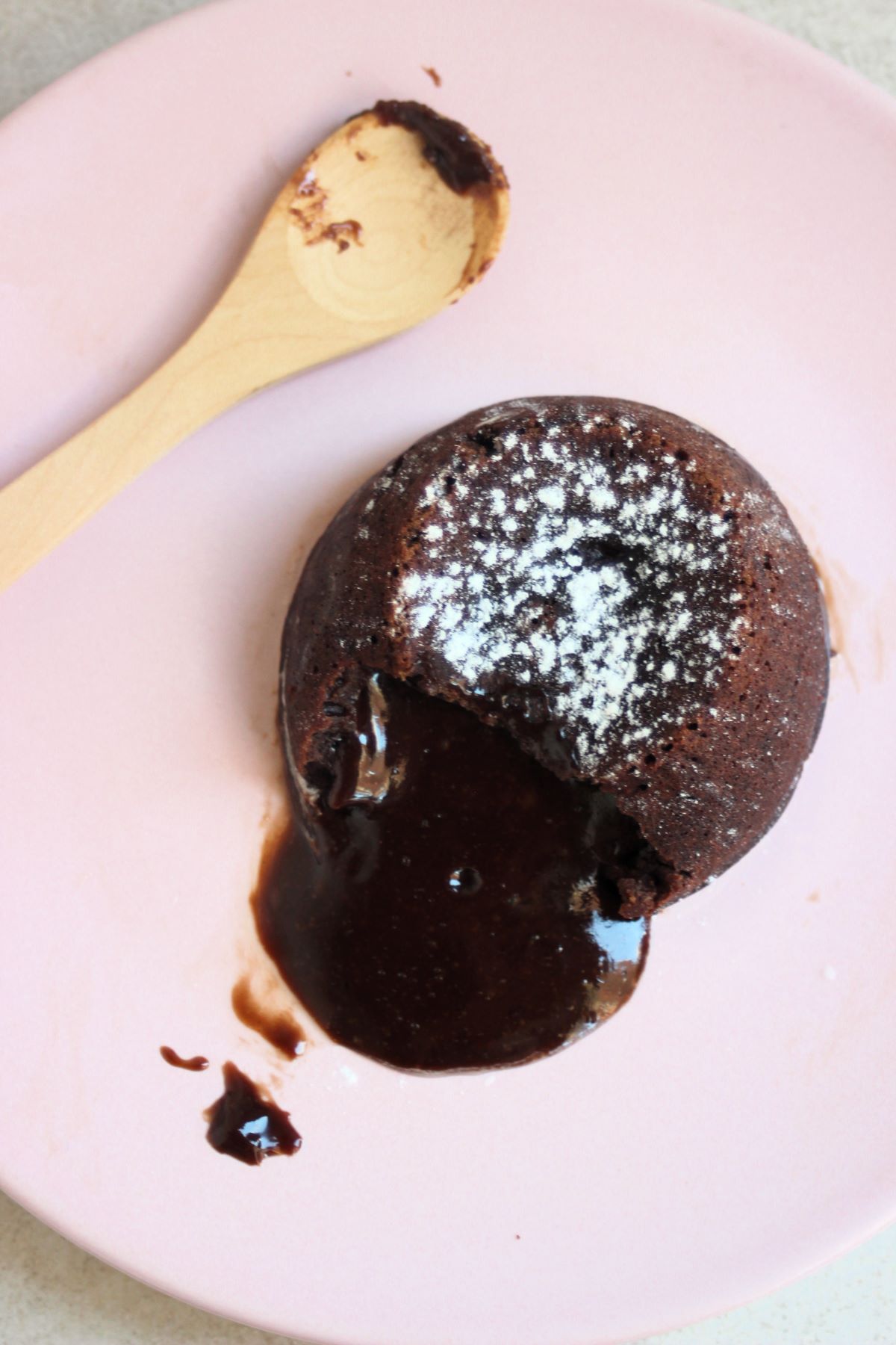 Molten lava cake, melted chocolate coming out of it, and a wooden spoon on a pink plate.