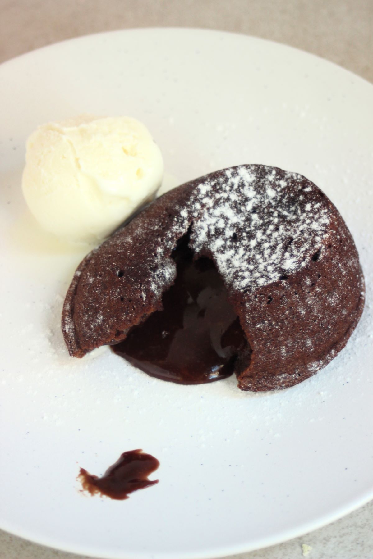 Molten lava cake, melted chocolate coming out of it, and a scoop of ice cream on a white plate.