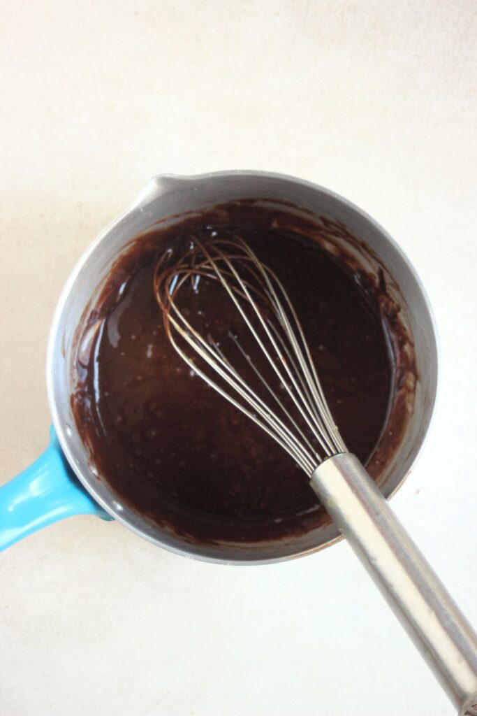 Deep saucepan with melted chocolate and a hand whisk.