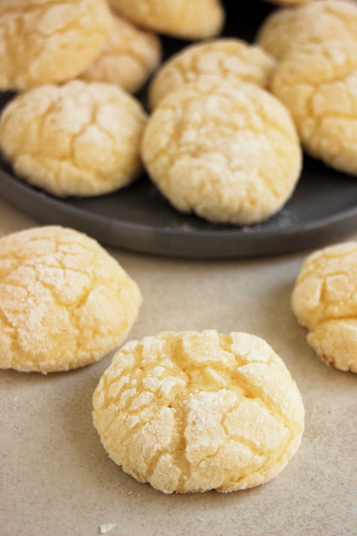 Lemon crinkle cookies on a white surface. More cookies behind on a gray plate.