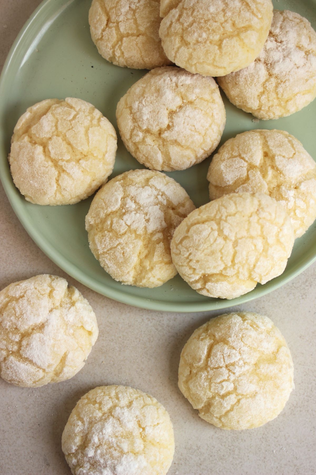 Lemon crinkle cookies on a plate and more cookies beside seen from above.