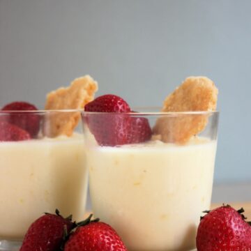 Glass cup with lemon posset, strawberries, and shortcake cookie. Strawberries on the side.