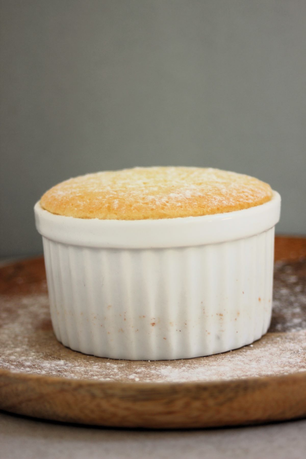 White ramekin with lemon pudding cake on a wooden plate.