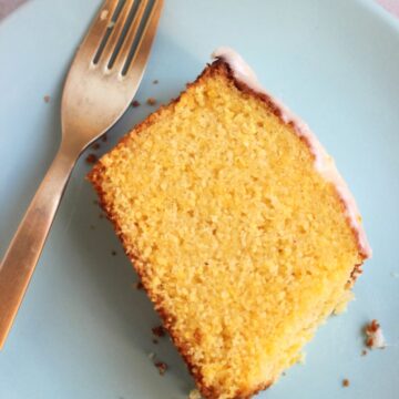 A slice of orange cake with icing on a light blue plate and a golden fork.