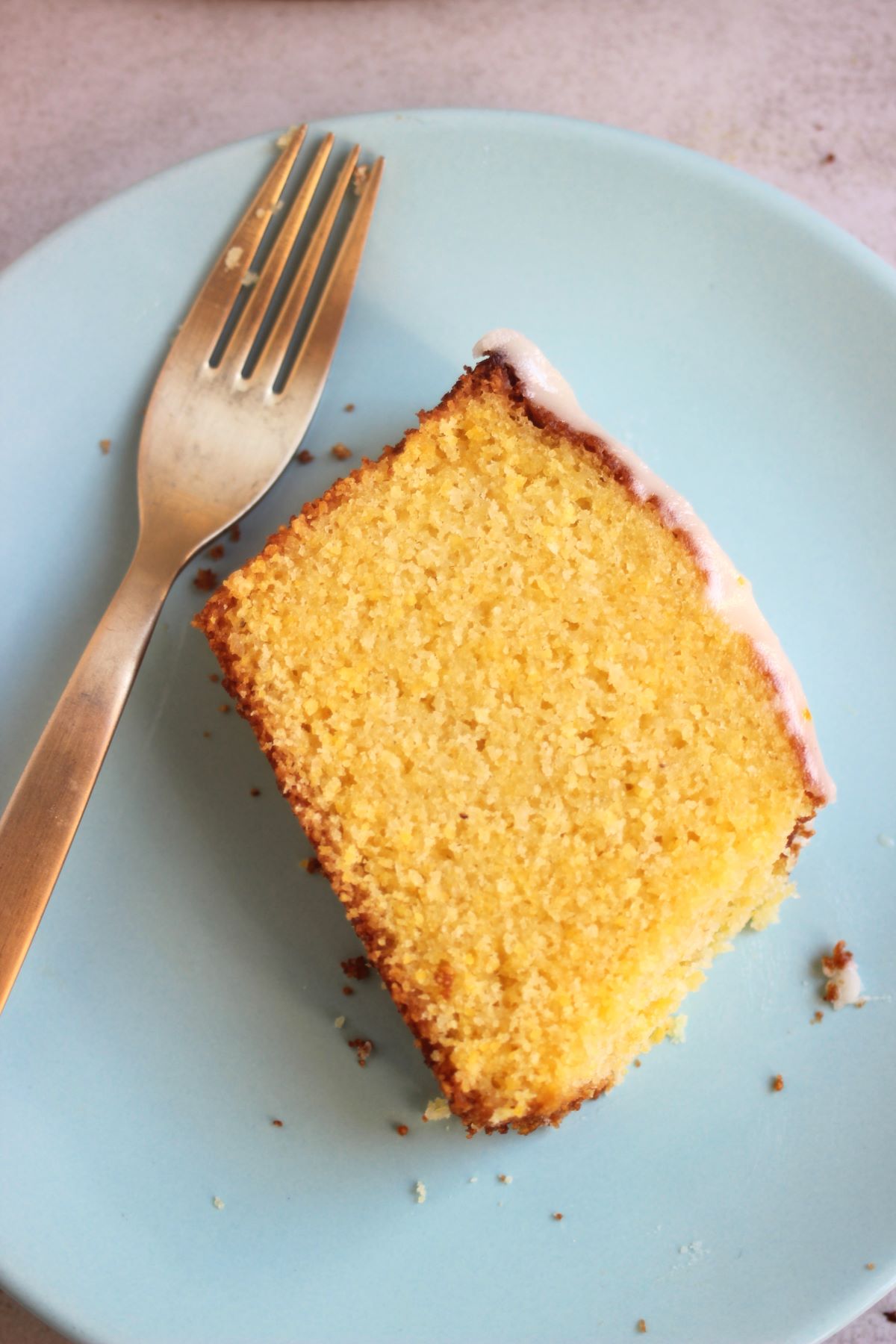 A slice of orange cake with icing on a light blue plate and a golden fork.