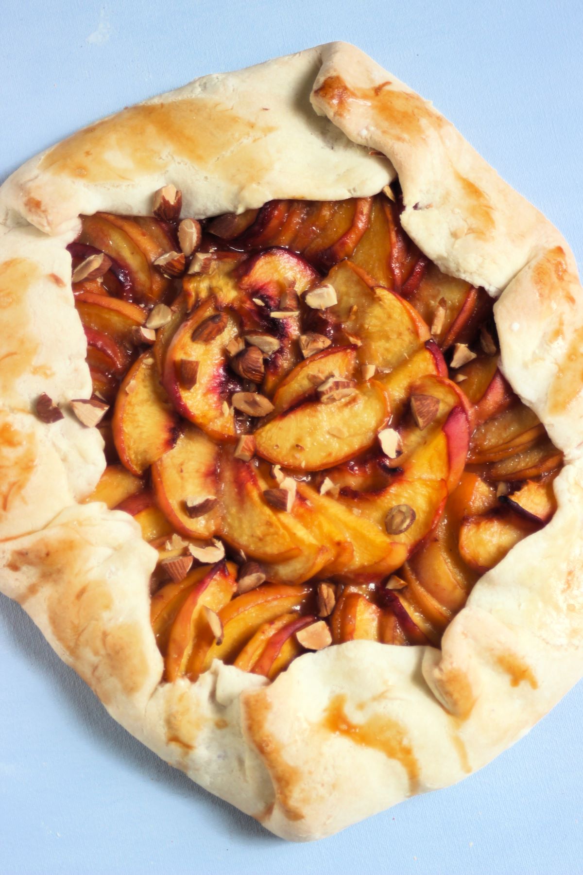 Peach galette on a light blue surface seen from above.