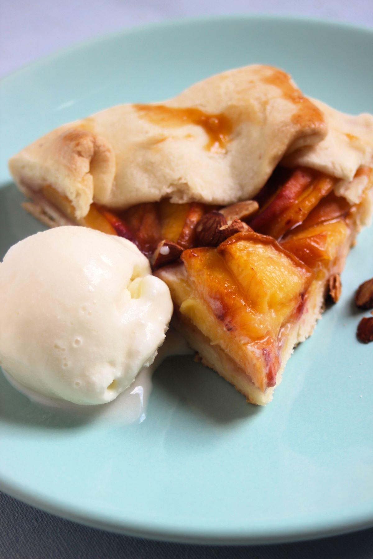 Portion of peach galette and a scoop of ice cream on aqua green plate.