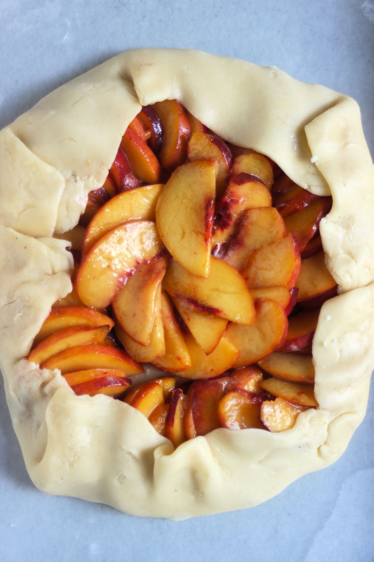 Raw peach galette on a parchment paper.