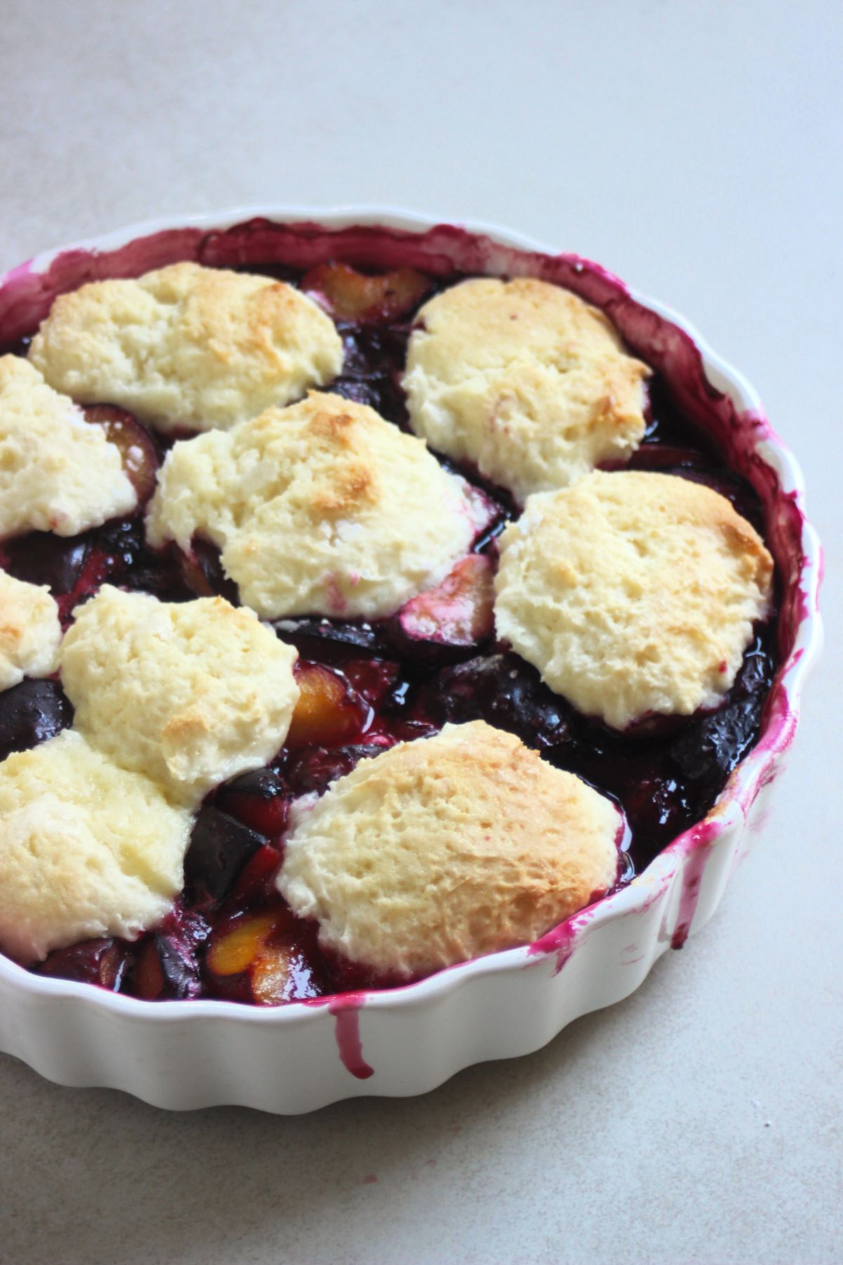 Round baking pan with plum cobbler on a white surface.