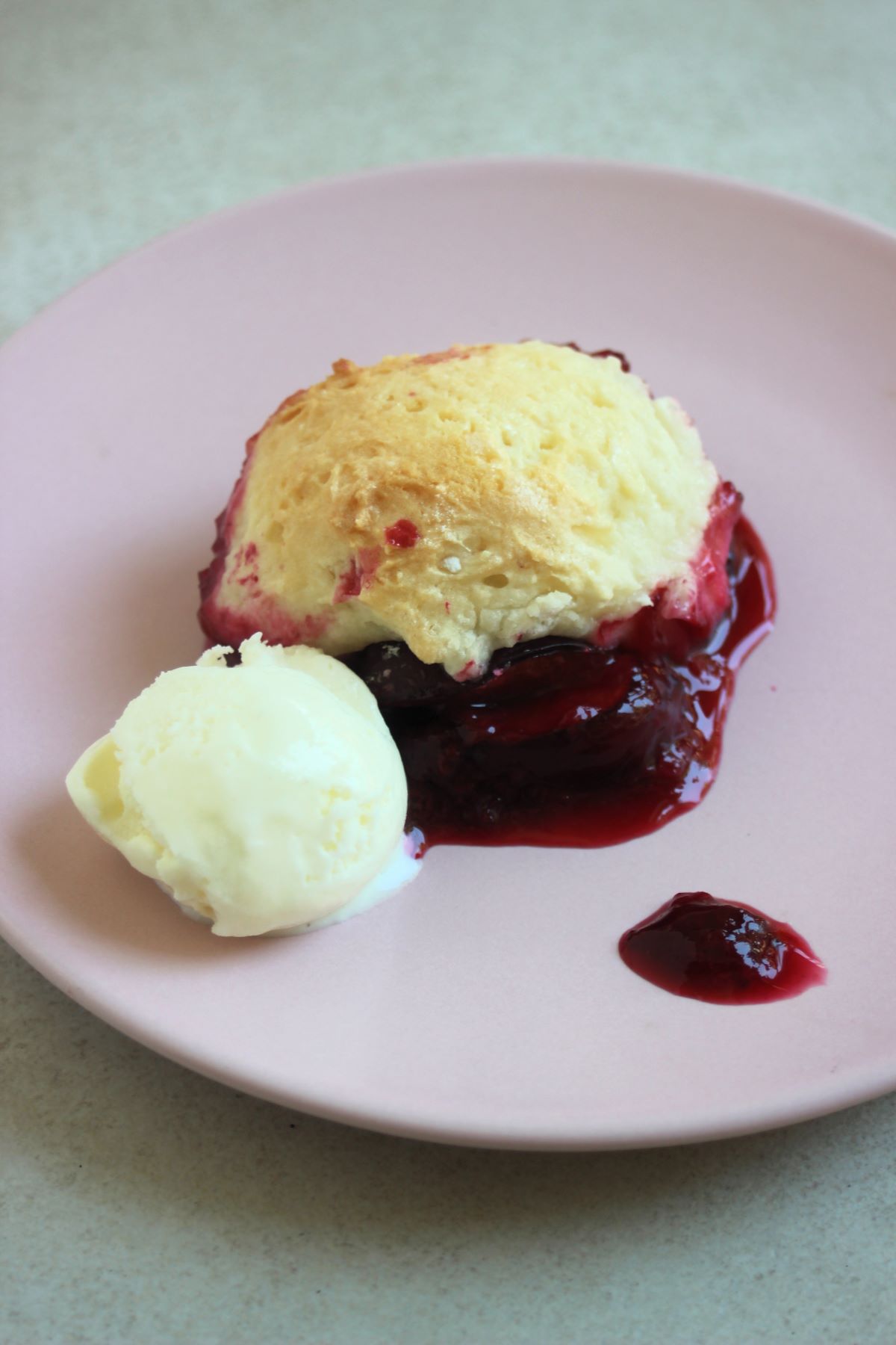 A portion of plum cobbler and a scoop of ice cream on a pink plate.