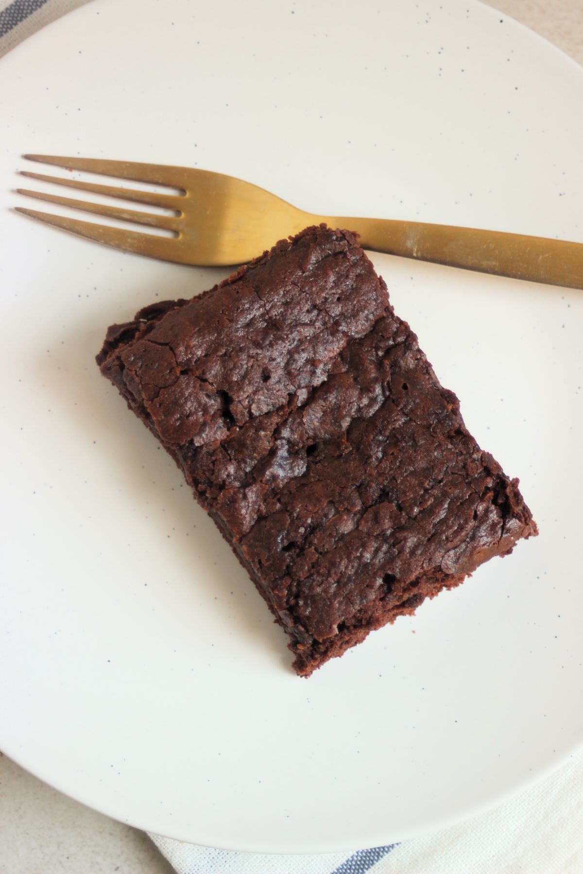Brownie and a golden fork on a white plate seen from above.