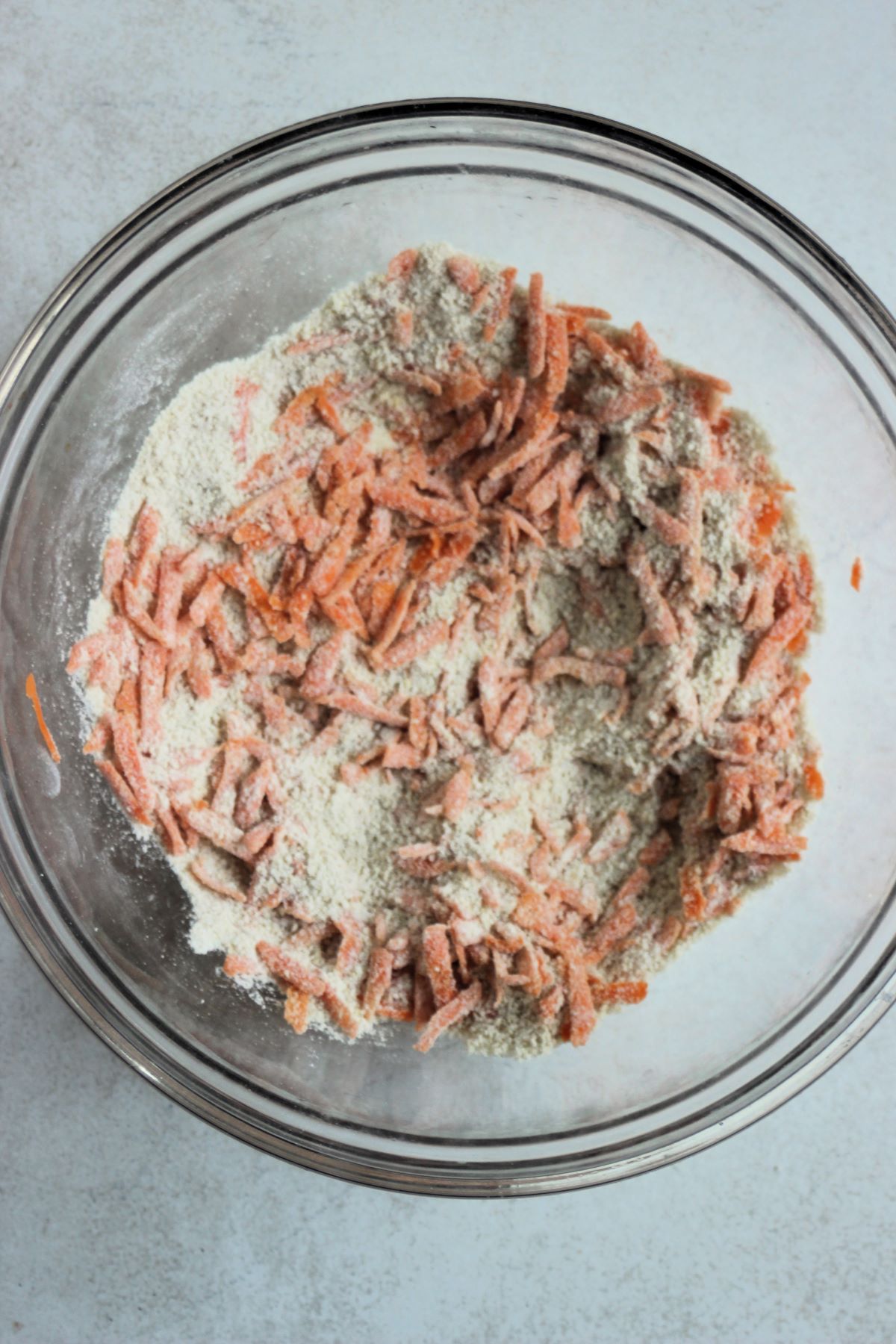 Glass bowl with a flour mixture and grated carrots.
