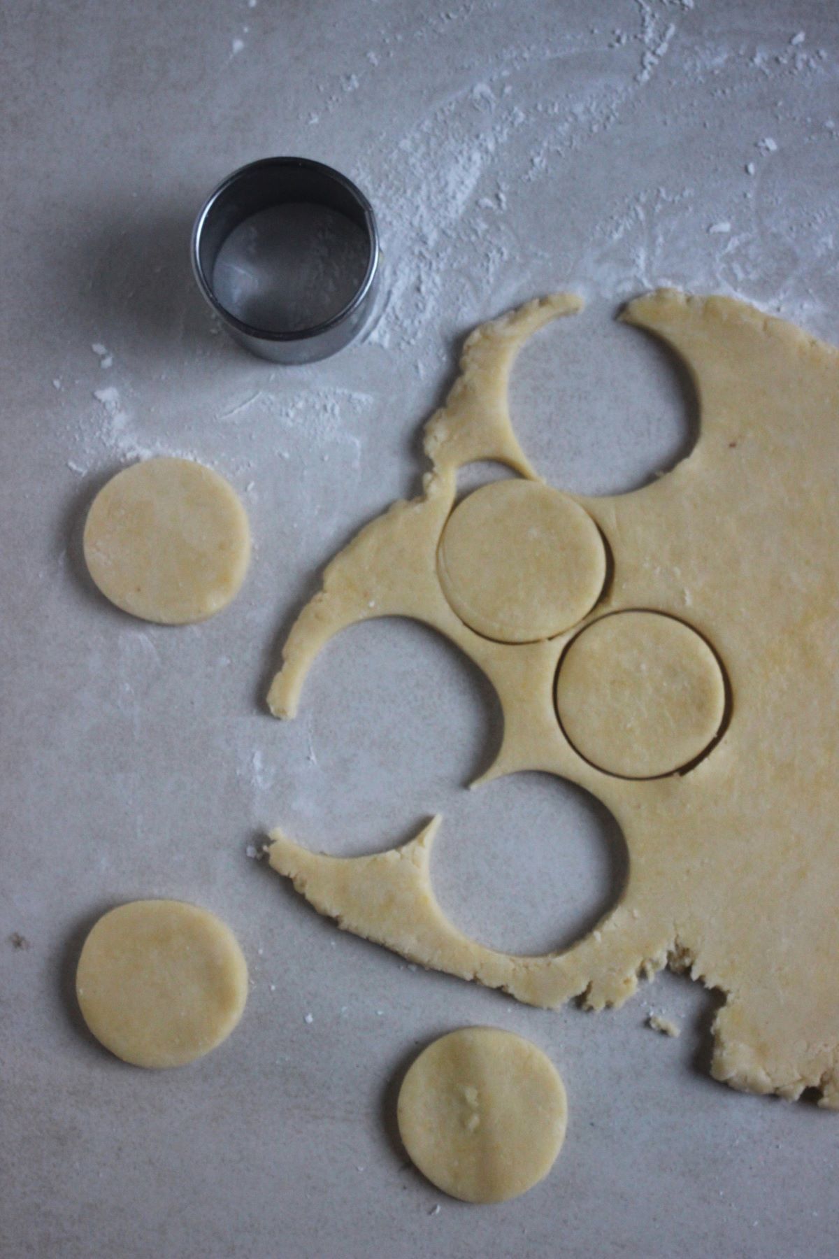 Alfajor dough stretched on a white surface, a cutter, and rounds of alfajor dough cut.