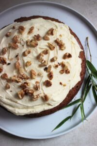 Sweet potato cake with cream cheese frosting and chopped nuts on a white plate seen from above,