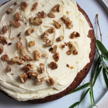 Sweet potato cake with cream cheese frosting and chopped nuts on a white plate seen from above,