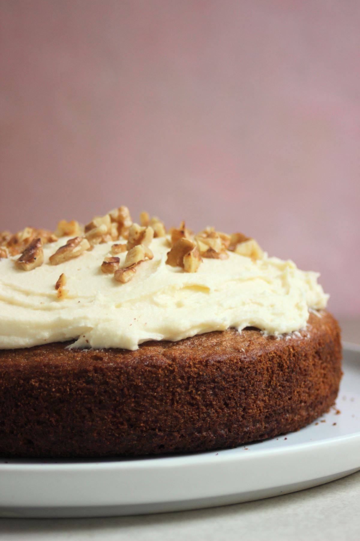 Sweet potato cake with cream cheese frosting and chopped nuts front view on a white plate.
