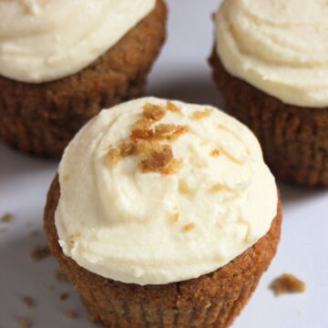 Sweet potato muffins with cream cheese frosting on a white surface.