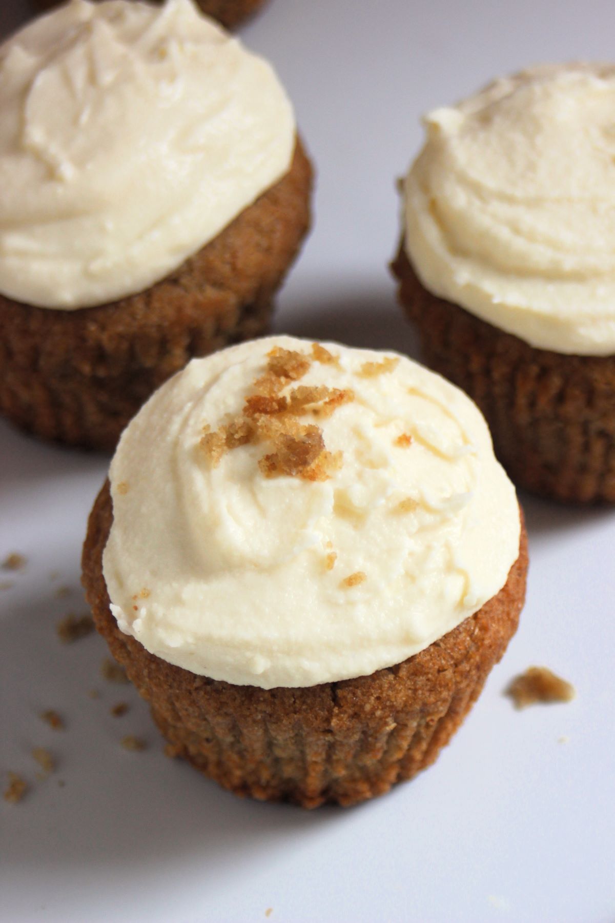 Sweet potato muffins with cream cheese frosting on a white surface.