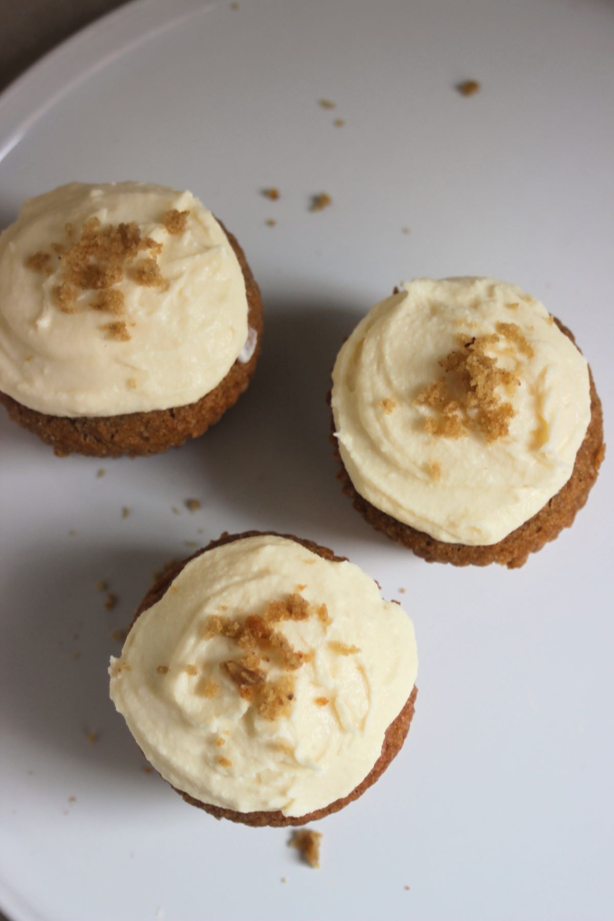 Sweet potato muffins with cream cheese frosting on a white surface seen from above.