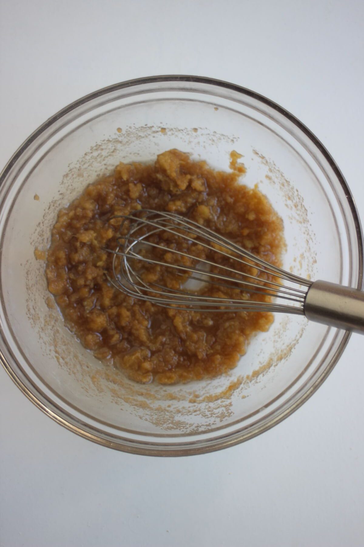 Glass bowl with a brown mixture and a hand whisk.