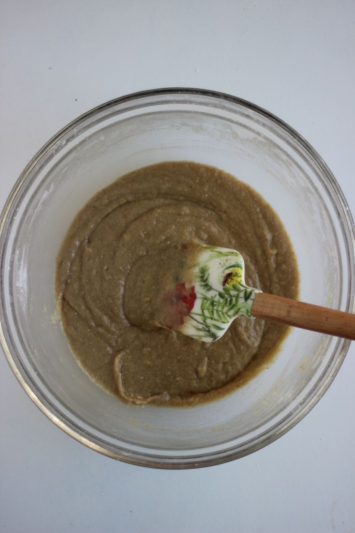 Glass bowl with a smooth brown mixture and a rubber spatula.