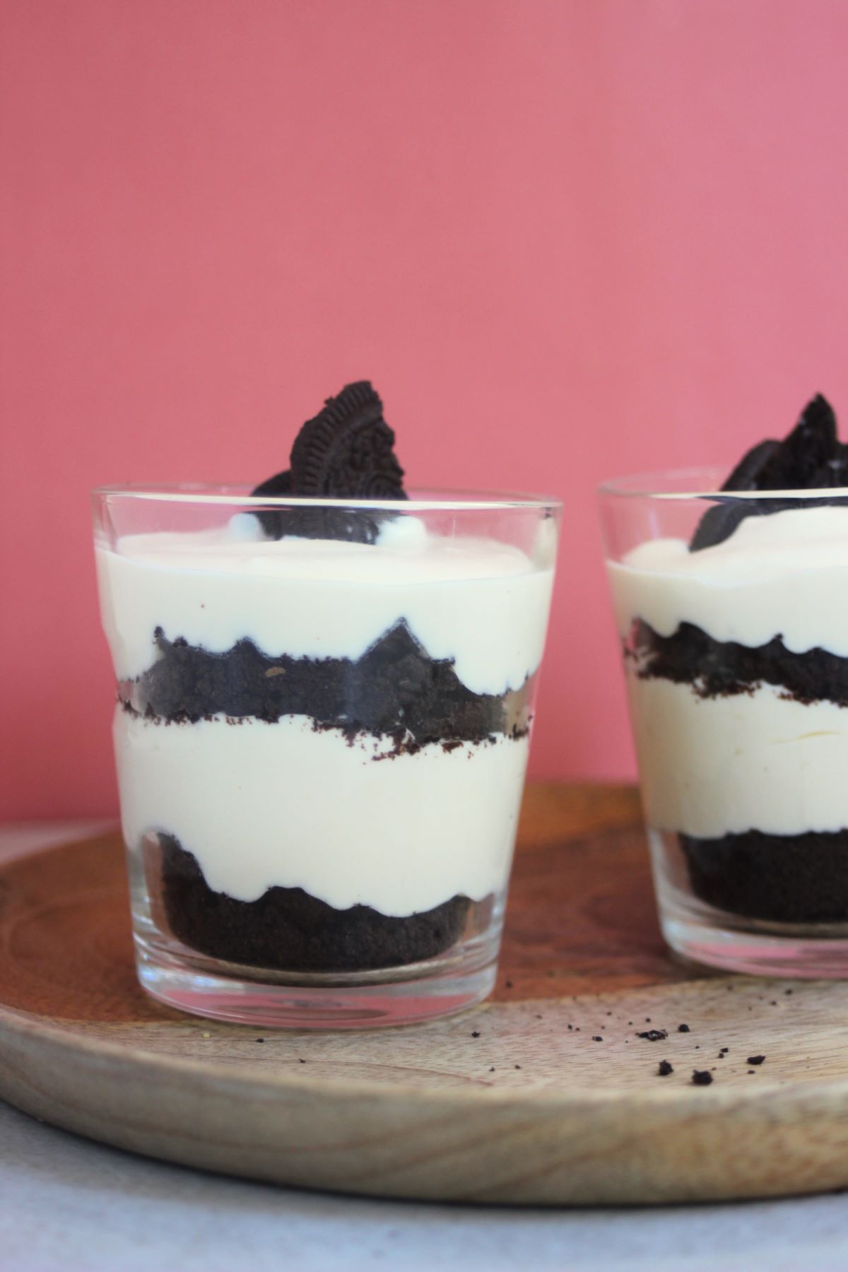 Two glasses with lemon mousse and Oreos on a wooden plate. Pink background.