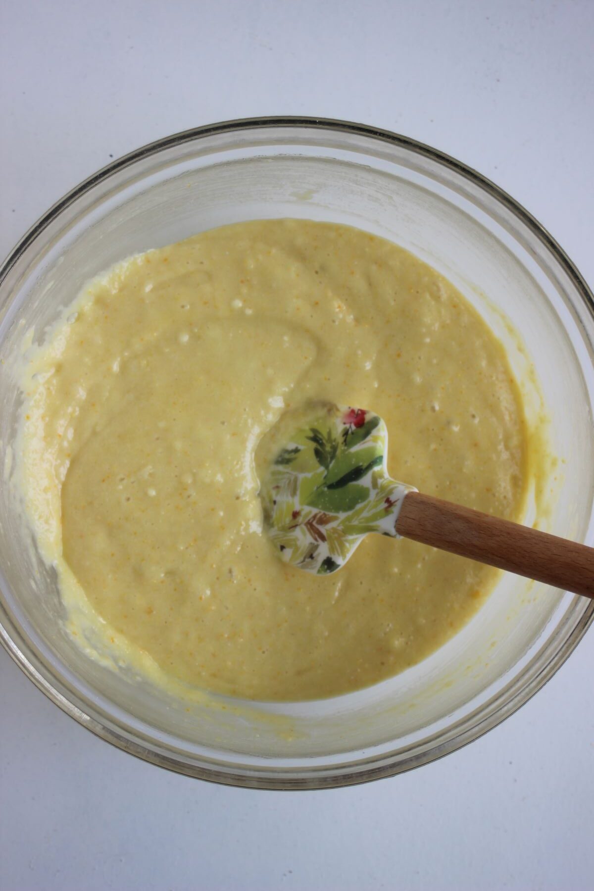 GLass bowl with a light yellow mixture and a rubber spatula.